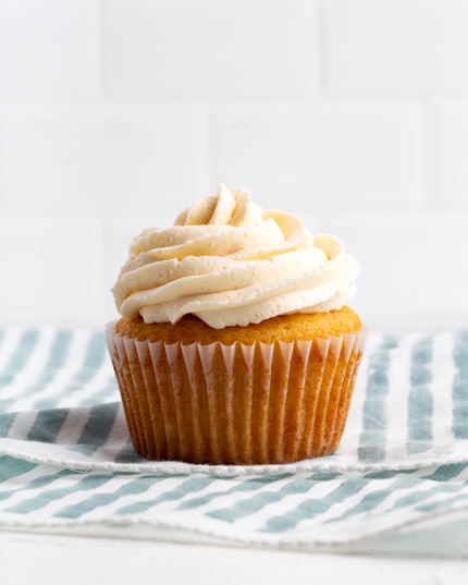 A vanilla cupcake topped with buttercream icing on a striped tea towel
