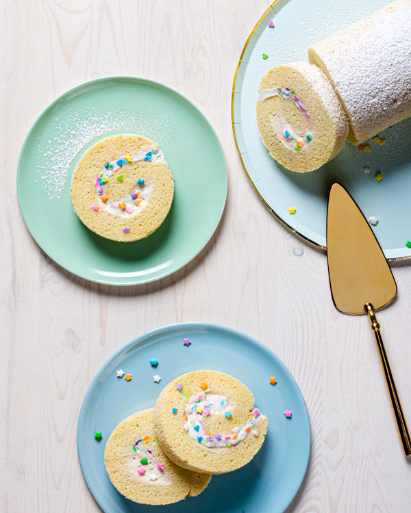 White cake roll on a plate with four slices cut, shown on pastel plates with a gold cake server.