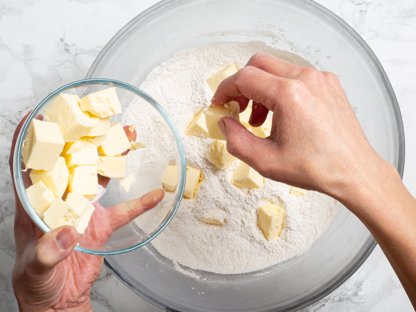 Dropping cubes of cold butter into a bowl of flour, sugar, and salt