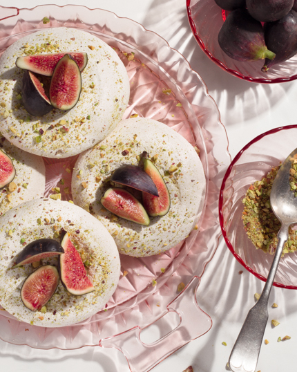 Meringues on a glass dish, topped with pistachio and figs