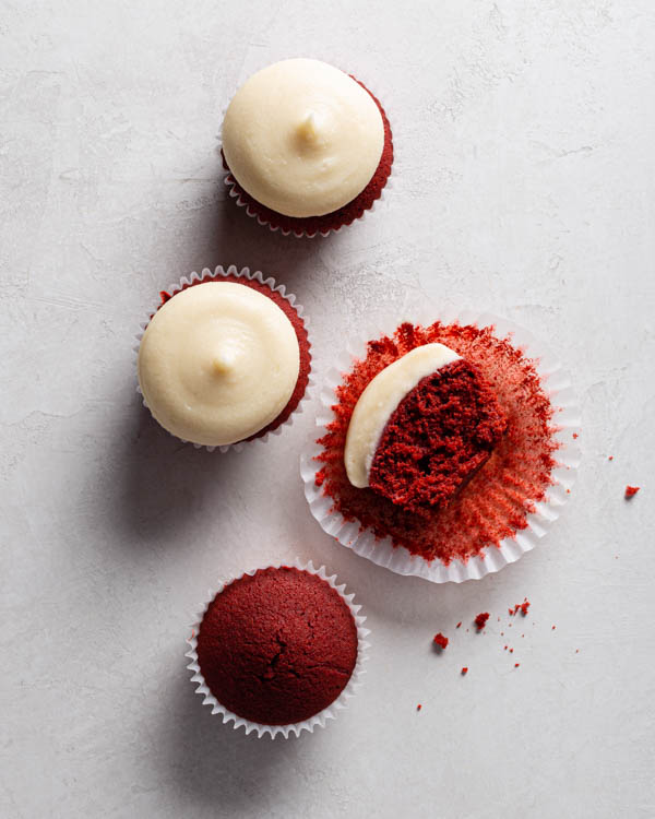  Four Red Velvet Cupcakes with Cream Cheese Frosting on a counter, one without icing and one cut in half