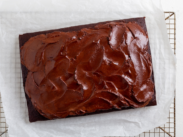 Iced vegan chocolate cake on parchment paper on a wire cooling rack