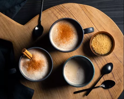 Three mugs of hot horchata garnished with cinnamon sticks and powdered cinnamon