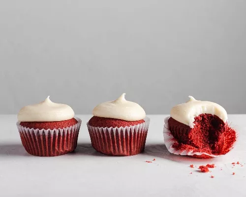 Three Red Velvet Cupcakes with Cream Cheese Frosting lined up, one with the liner peeled and a bite missing