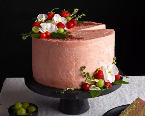 White Wine Celebration Cake on a cake platter with strawberries, flowers and a slice missing