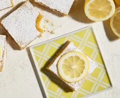 Lemon square on a yellow squared plate with slices of lemon