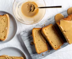 Slices of glazed beer cake on a marble slab with a bowl of glaze and two plated slices