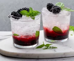 Two blackberry gin fizz cocktails garnished with blackberries and mint leaves on a platter