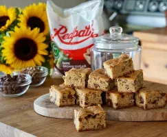 Brown Butter Blondies with chocolate chips on a butcher block counter with sunflowers and a bag of Redpath Dark Brown Sugar