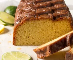 A loaf of pound cake sliced at one end, on a plate with sliced lemons and limes