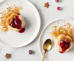 Two gingerbread panna cotta topped with cranberries on white plates with a gold spoon