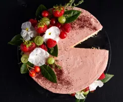 Pink Swiss meringue buttercream frosted cake on a cake stand decorated with flowers, greenery, and berries