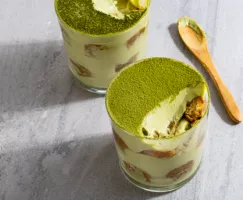 Two glass cups of tiramisu sprinkled with green matcha powder