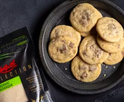 Milk chocolate chunk sugar cookies on a black plate with a black napkin on a black slate counter