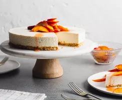 No-bake vanilla cheesecake with peach topping on a cake stand with a slice served on a plate.