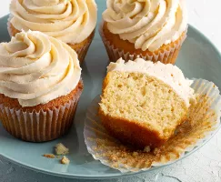 Four iced vanilla cupcakes on a plate, one cut in half