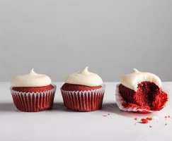 Three Red Velvet Cupcakes with Cream Cheese Frosting lined up, one with the liner peeled and a bite missing