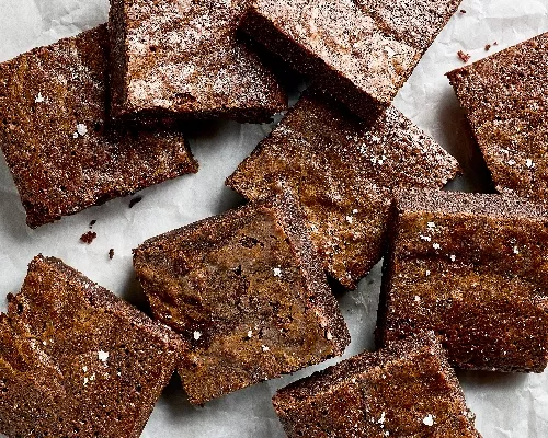 Six square brownies decorated for Halloween like jack o’lanterns, mummies, and Frankenstein, shown on a black plate with bones scattered around